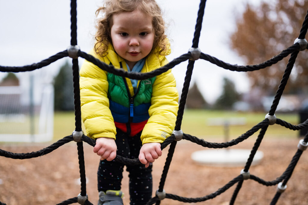 Photograph of a toddler girl climbing cargo netting.